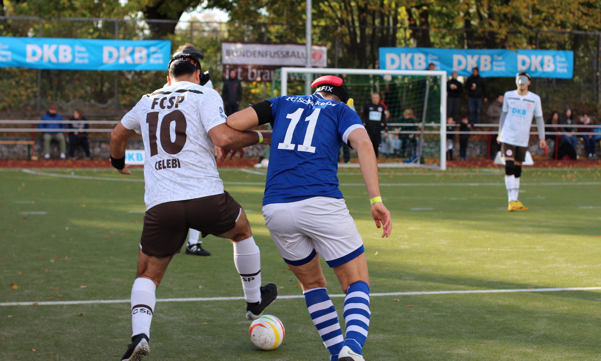 Spielszene im Mittelfeld Serdal Celebi führt den Ball dynamisch in Richtung Mittellinie. Er wird von Hasan Koparan verfolgt. Beide Spieler sind vom Rücken aus zu sehen. Im Hintergrund stehen weitere Spieler auf einem Kunstrasenplatz am Hamburger Borgweg, Foto: Tomke Koop.