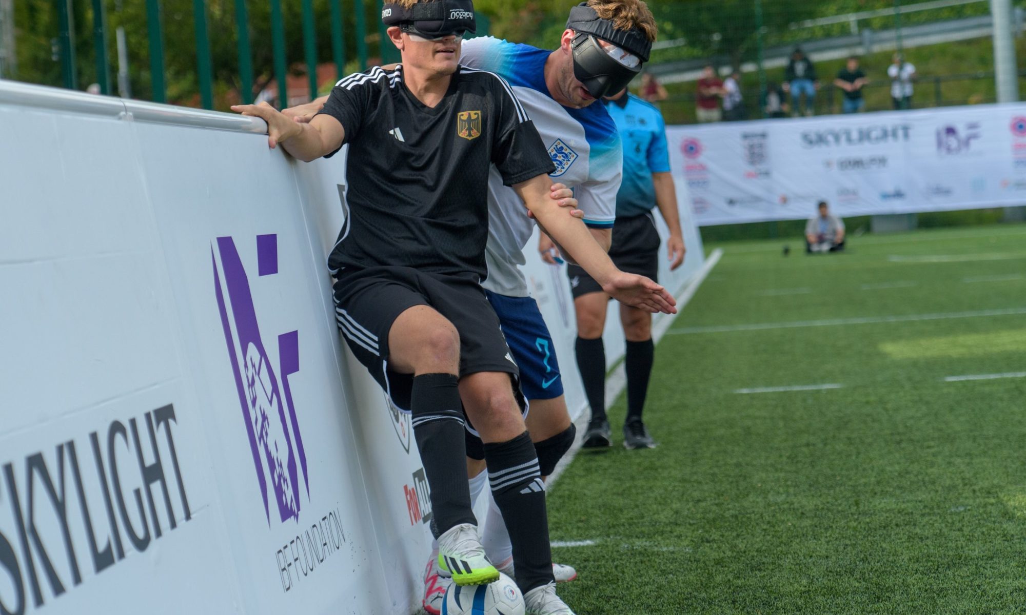 Deutschland gewann das Auftaktspiel gegen England bei der Blindenfußball-WM gegen England mit 1:0. Hier behauptet sich Deutschlands Taime Kuttig an der Seitenbande gegen einen englischen Spieler. Foto: Will Cheshire.